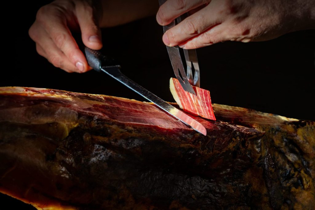 Manos de un profesional cortando una fina loncha de jamón ibérico.