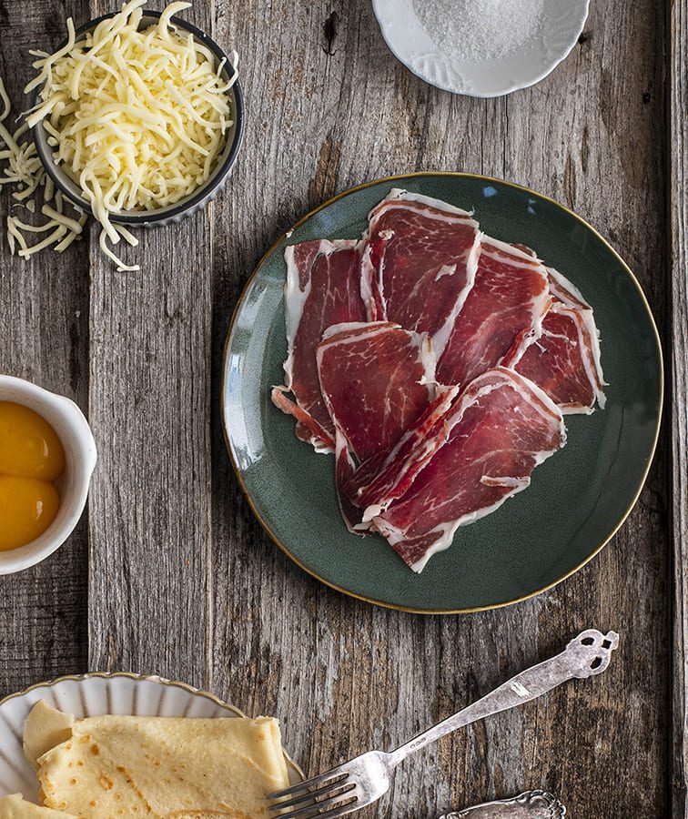 Plato de lonchas de jamón acompañado de queso y crepes.